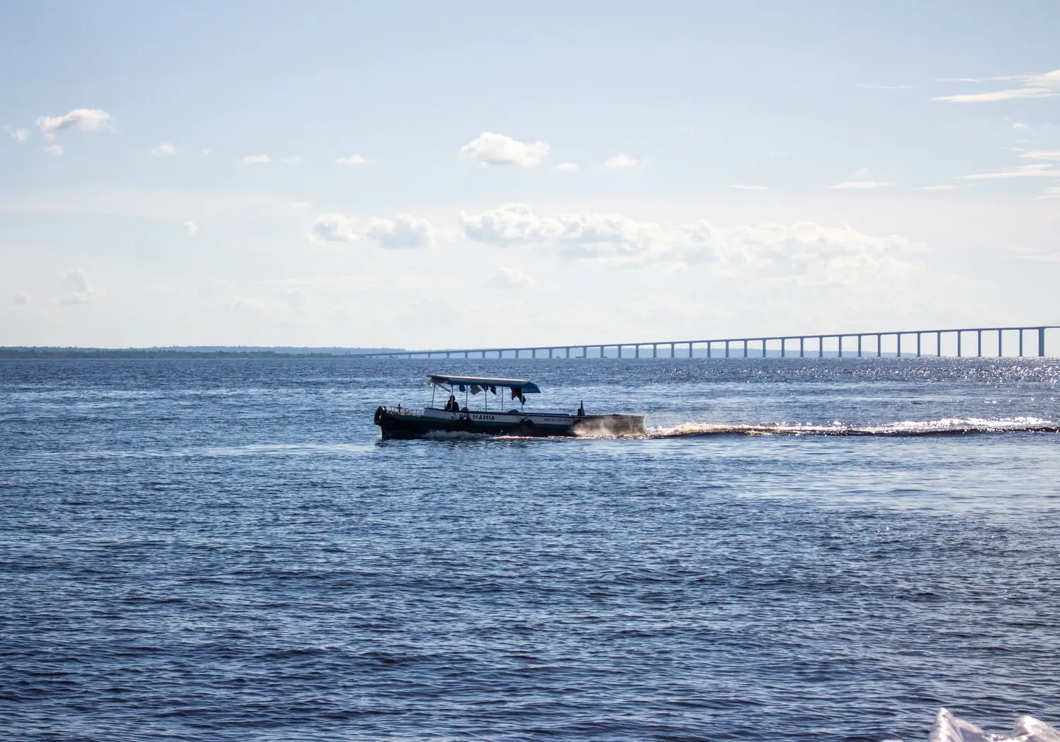 En båt på den breda Rio Negro med bron vid Manaus i bakgrunden.