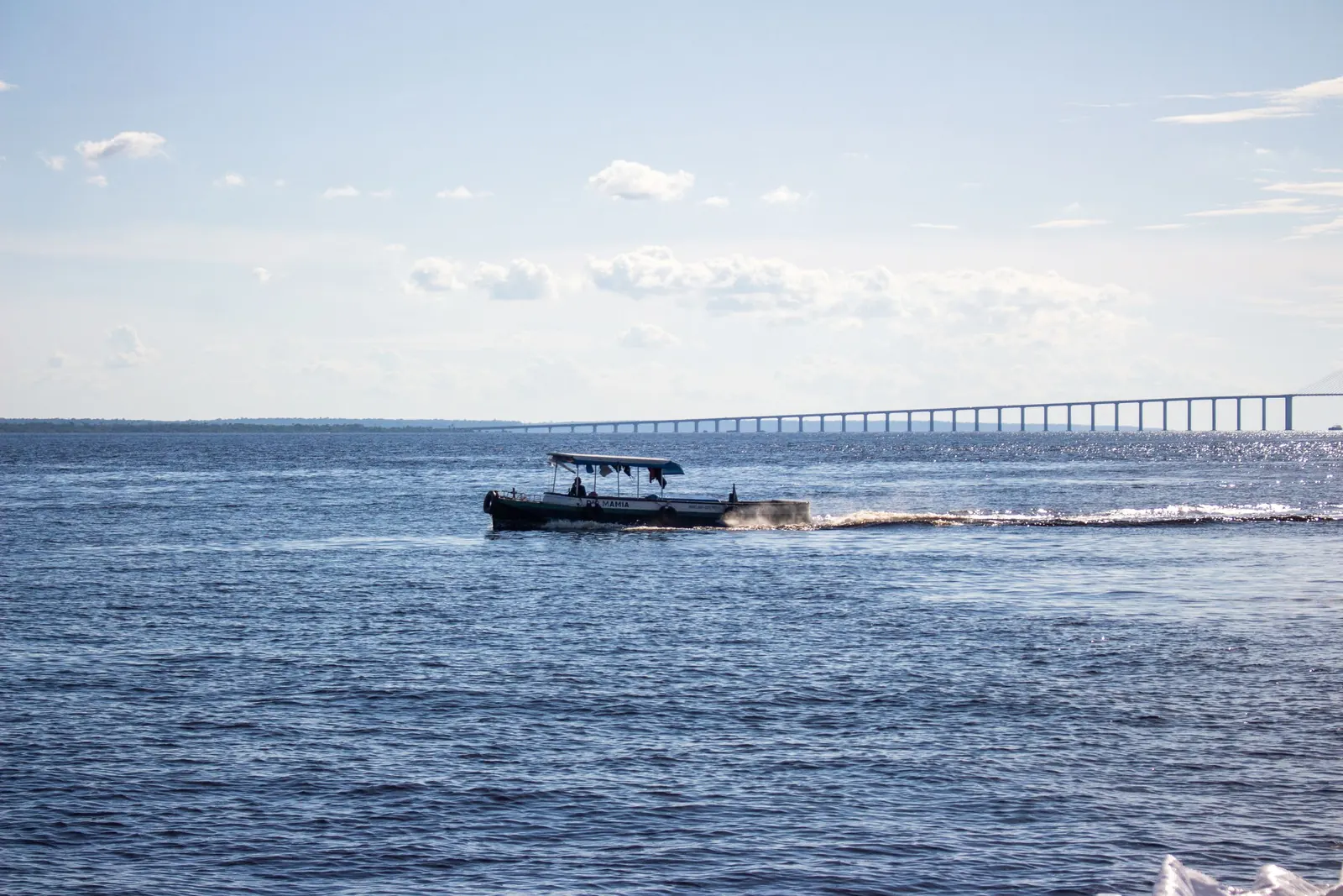 En båt på den breda Rio Negro med bron vid Manaus.